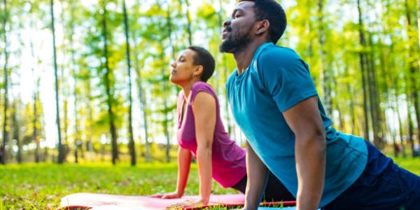 An attractive young woman and man doing yoga in green forest.
